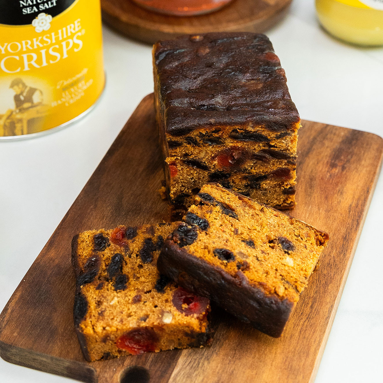 Rich sliced fruit cake on a wooden serving board, filled with raisins and cherries, presented as part of a luxury food hamper.