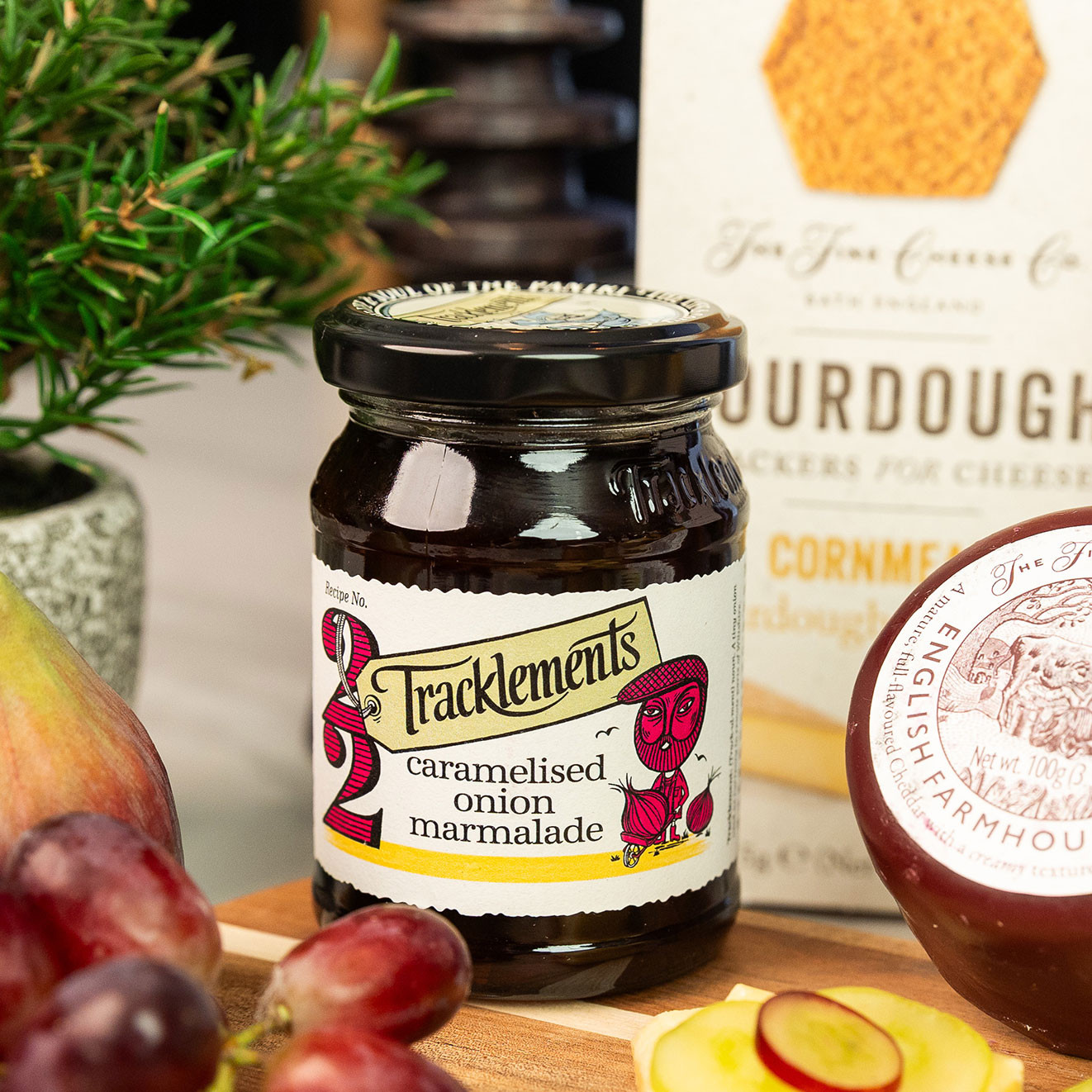 Jar of Tracklements Caramelised Onion Marmalade displayed with English farmhouse cheddar, sourdough crackers, grapes and fresh pear.