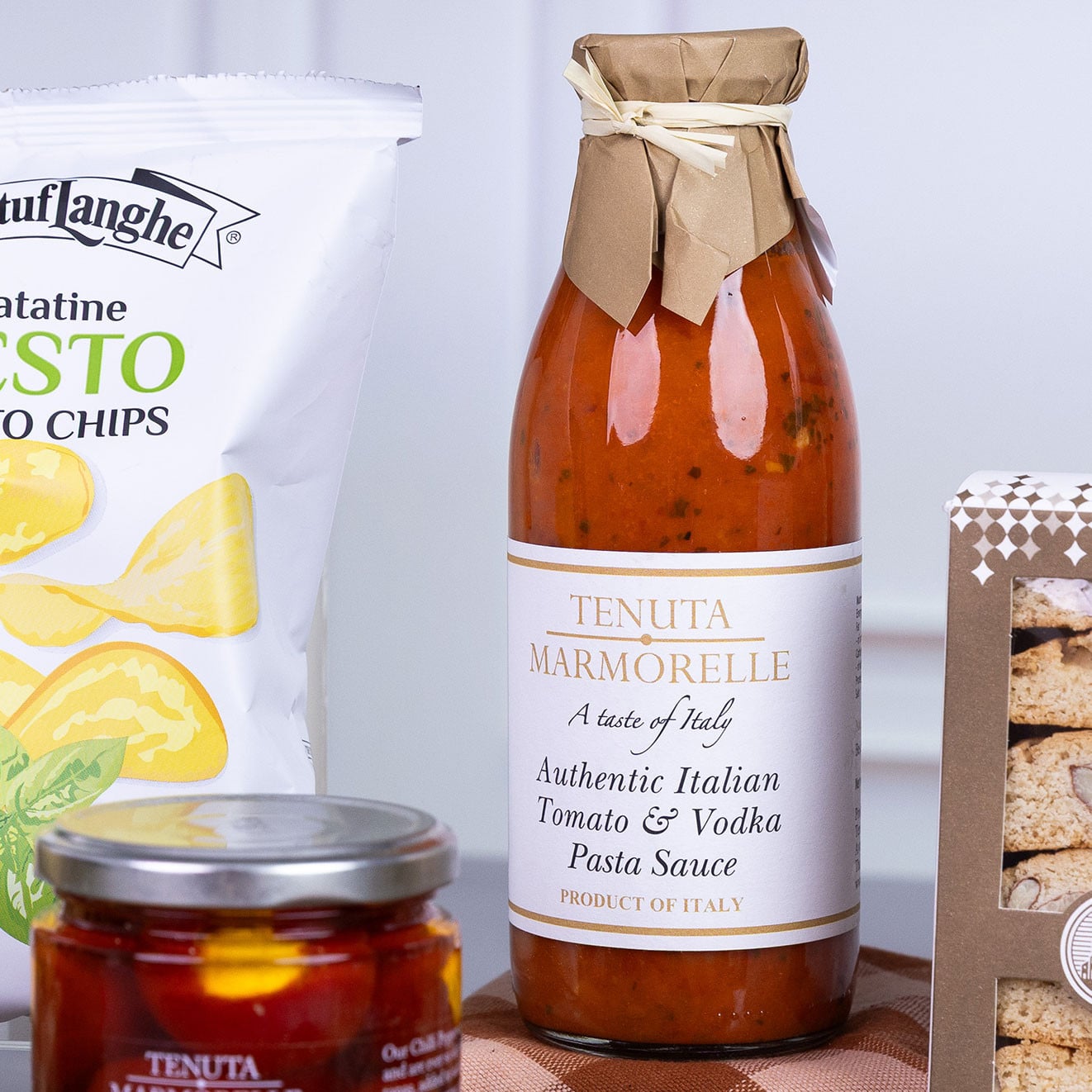 Bottle of Tenuta Marmorelle Authentic Italian Tomato & Vodka Pasta Sauce displayed with pesto potato chips, stuffed chilli peppers and artisan biscotti.