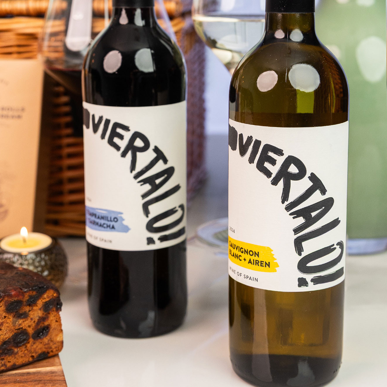 Bottles of Tempranillo Garnacha red wine and Sauvignon Blanc Airén white wine displayed beside filled wine glasses and treats.