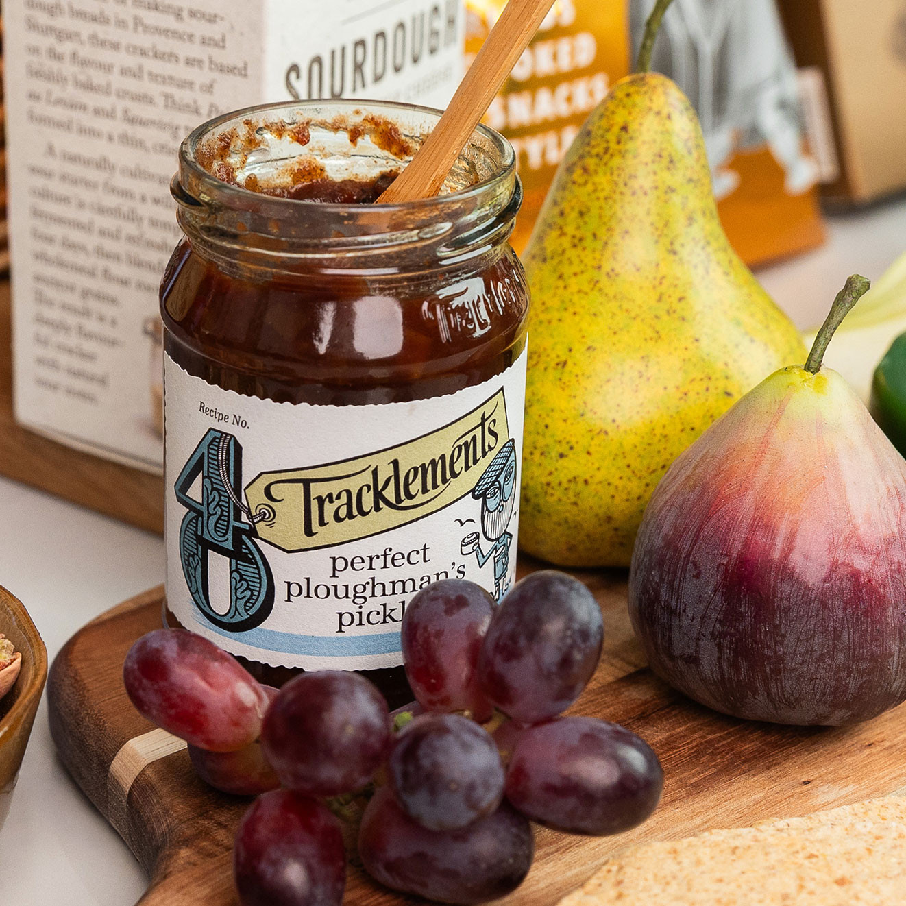 Tracklements Perfect Ploughman's Pickle served with fresh grapes, pear, fig and artisan crackers on a wooden serving board.