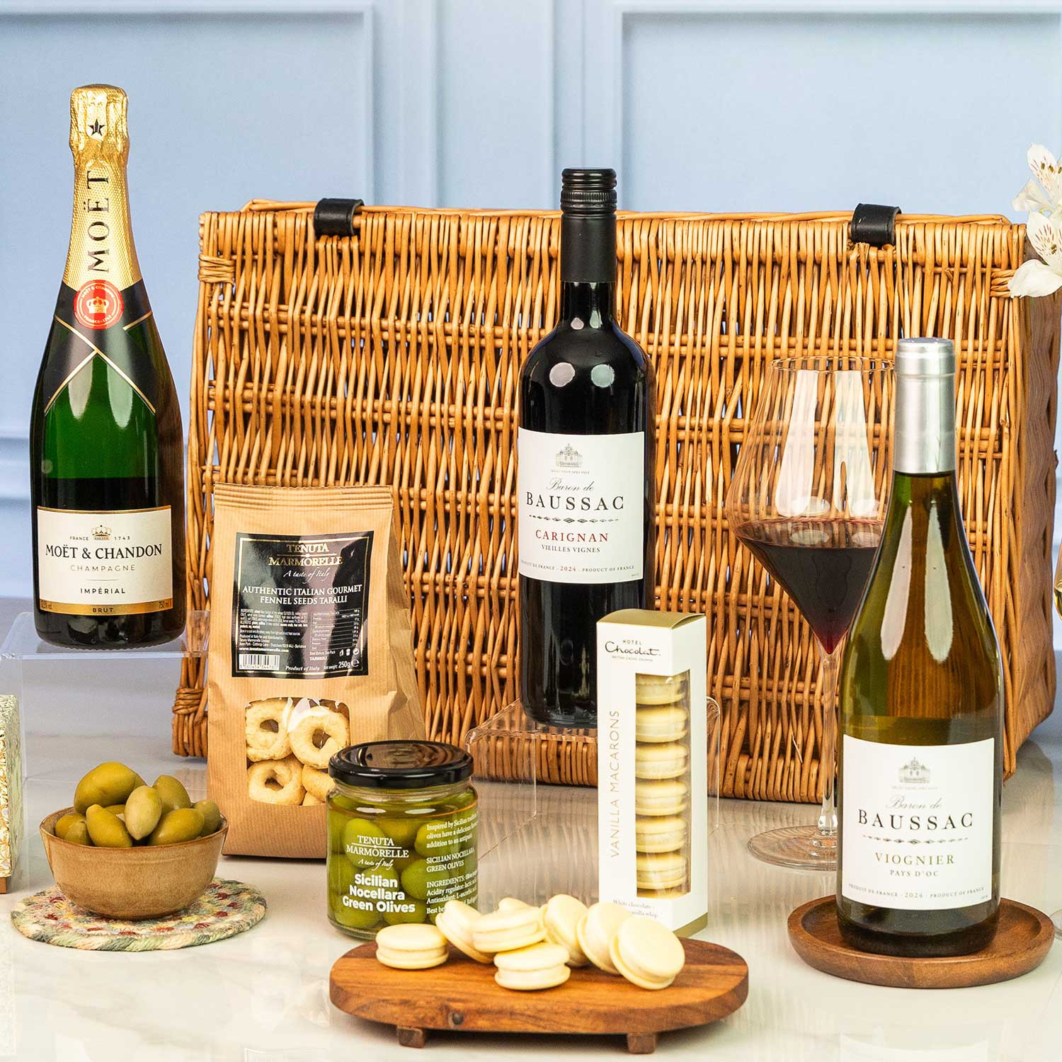 Close-up of the Luxury wicker hamper featuring Moët & Chandon Champagne, French red and white wine, Sicilian olives, artisan taralli, macarons, mint chocolates and gourmet sweet and savoury treats.