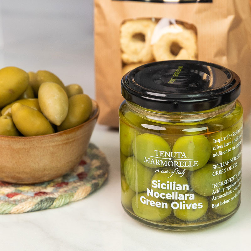 Jar of Tenuta Marmorelle Sicilian Nocellara Green Olives displayed beside a bowl of olives and artisan fennel seed taralli.