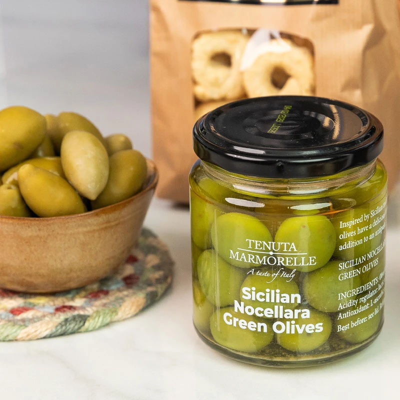 Jar of Tenuta Marmorelle Sicilian Nocellara Green Olives displayed beside a bowl of olives and artisan fennel seed taralli.