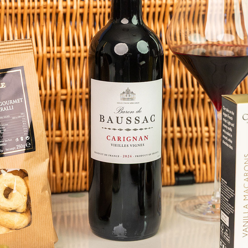 Bottle of Baron de Baussac Carignan Vieilles Vignes French red wine displayed beside a filled red wine glass and gourmet treats.