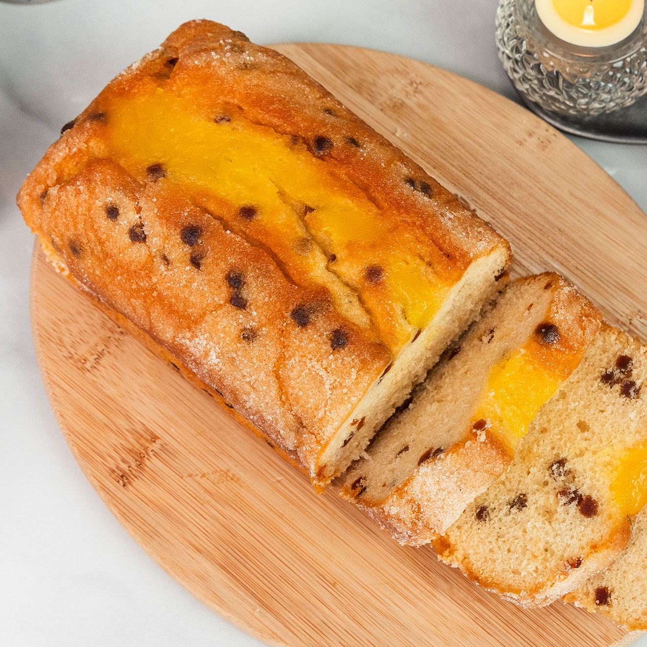 Traditional loaf cake studded with chocolate chips and topped with a rich golden glaze, served sliced on a wooden board.
