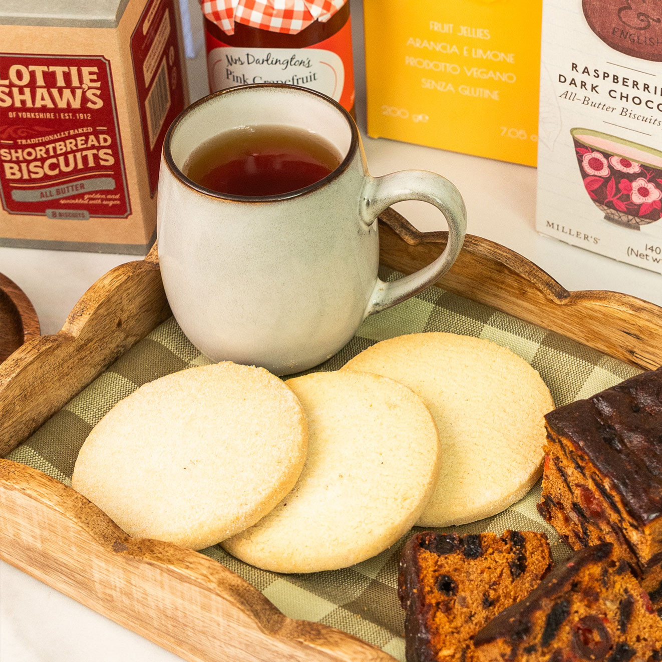 A mug of tea served with buttery shortbread biscuits and slices of rich fruit cake on a wooden serving tray.