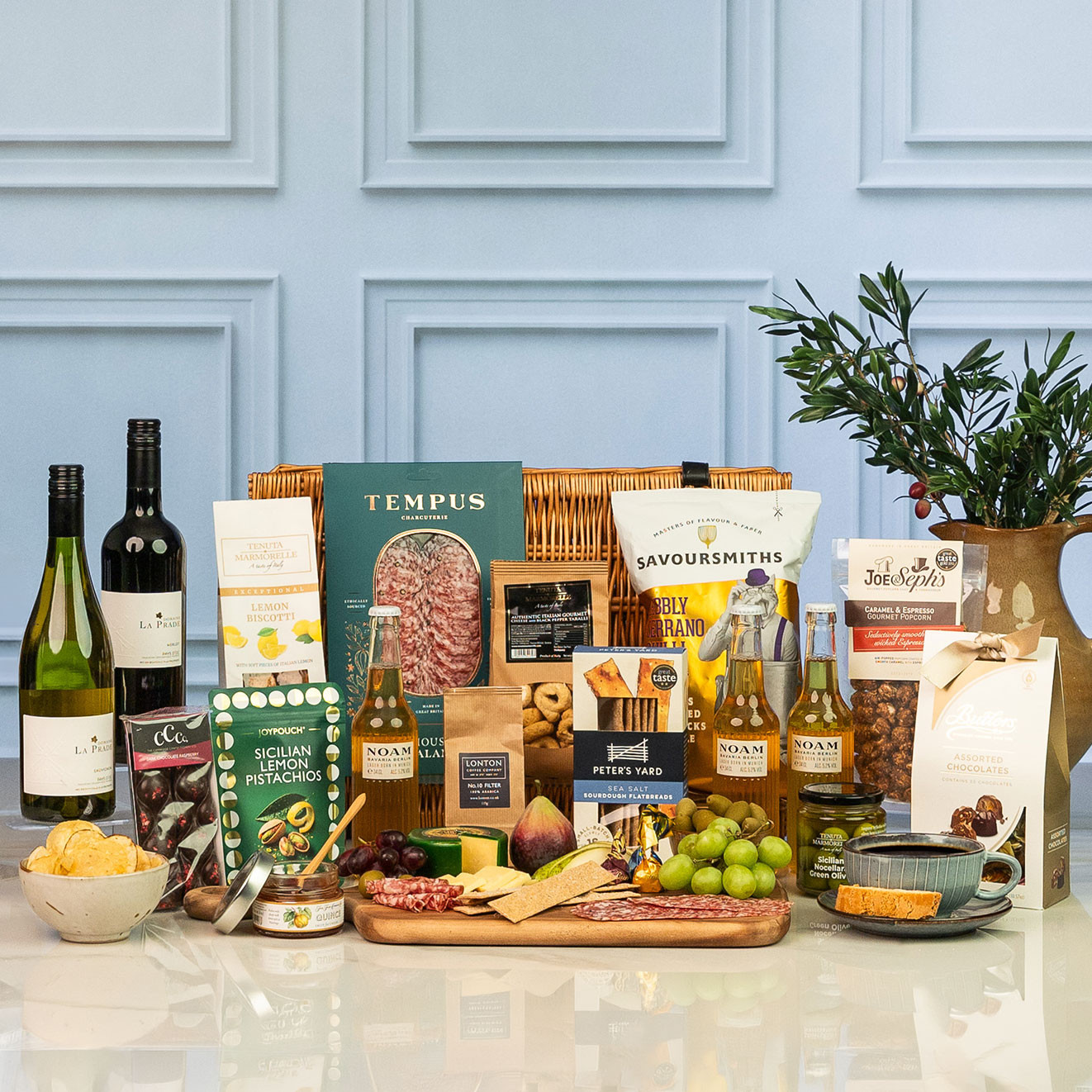 Square shot of luxury wicker hamper filled with premium wines, craft beers, artisan charcuterie, cheese, gourmet snacks, chocolates, olives and savoury treats.