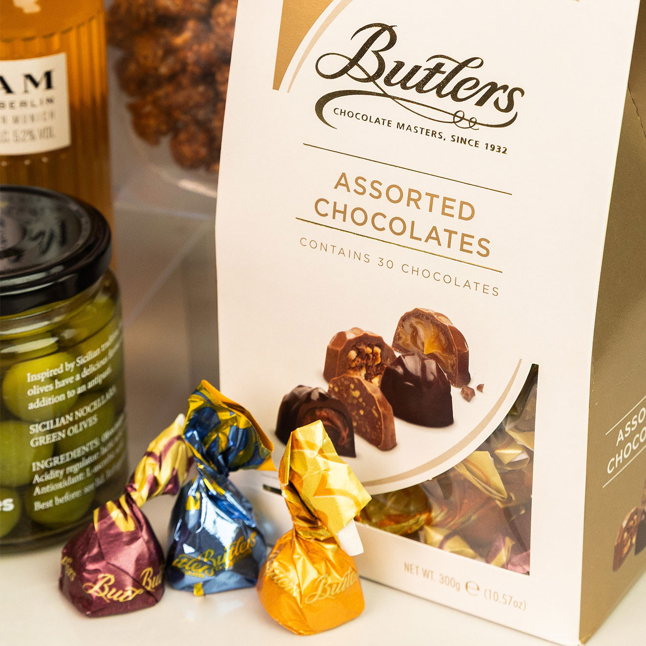 Butlers Assorted Chocolates gift box with individually wrapped chocolates, displayed alongside gourmet olives and craft beer.