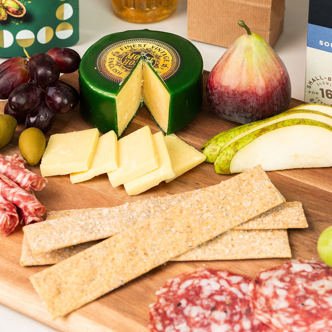 Vintage English cheese served with crackers, salami, grapes, olives, pear and fig on a rustic wooden grazing board.
