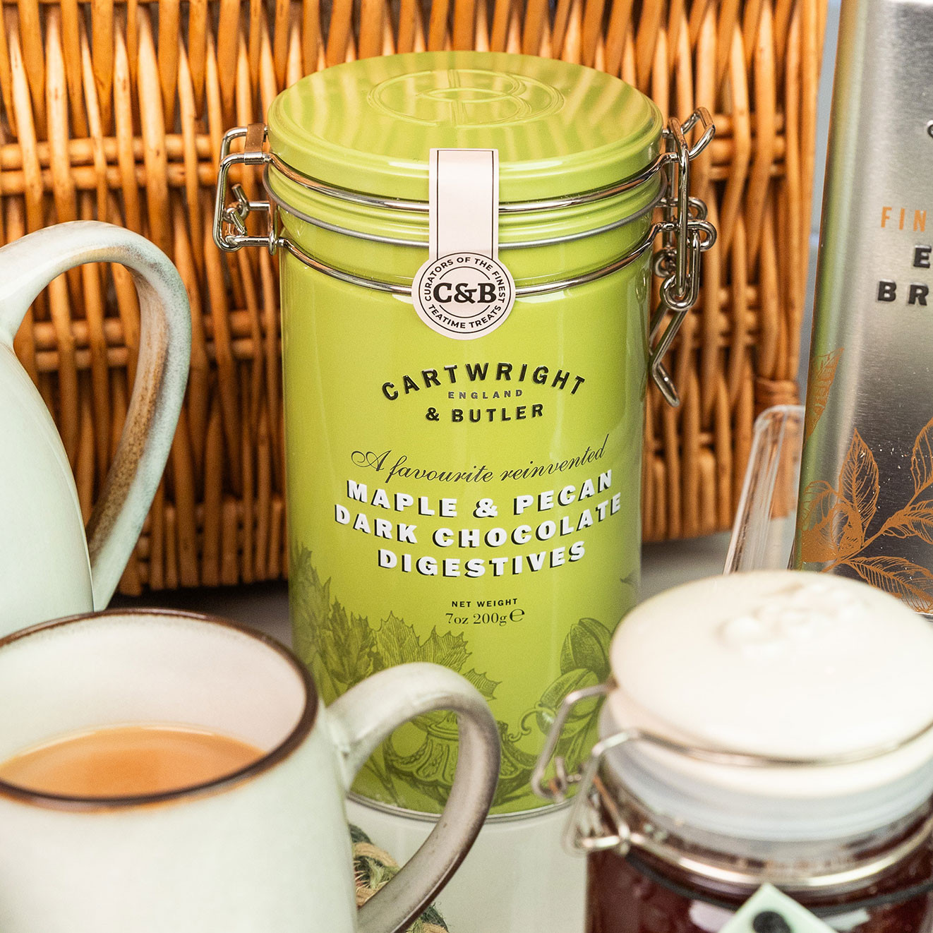 Cartwright & Butler Maple & Pecan Dark Chocolate Digestives presented in a decorative storage tin alongside artisan tea and coffee.