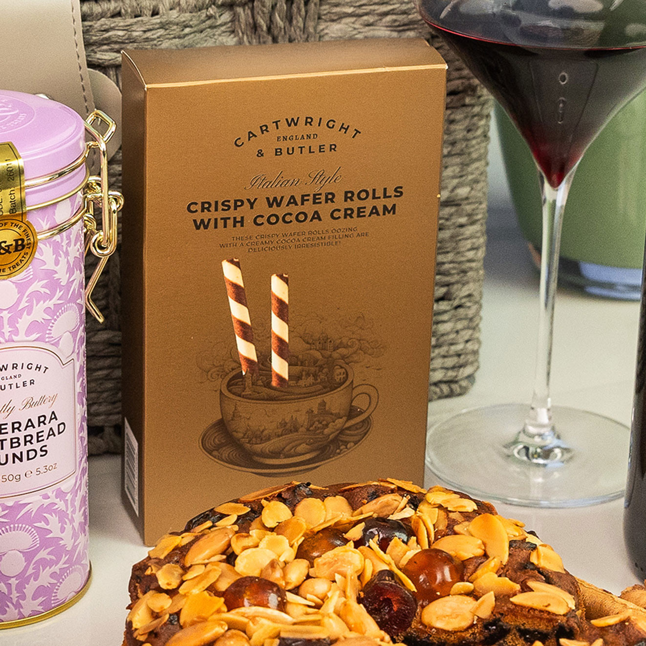 Cartwright & Butler Crispy Wafer Rolls with Cocoa Cream presented beside an almond-topped fruit cake and a glass of red wine.