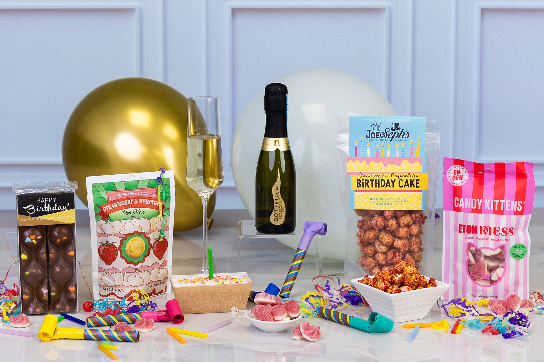 Birthday gift hamper featuring Bottega Prosecco, birthday cake popcorn, chocolates, sweets, dessert biscuits and celebratory treats with colourful party decorations.