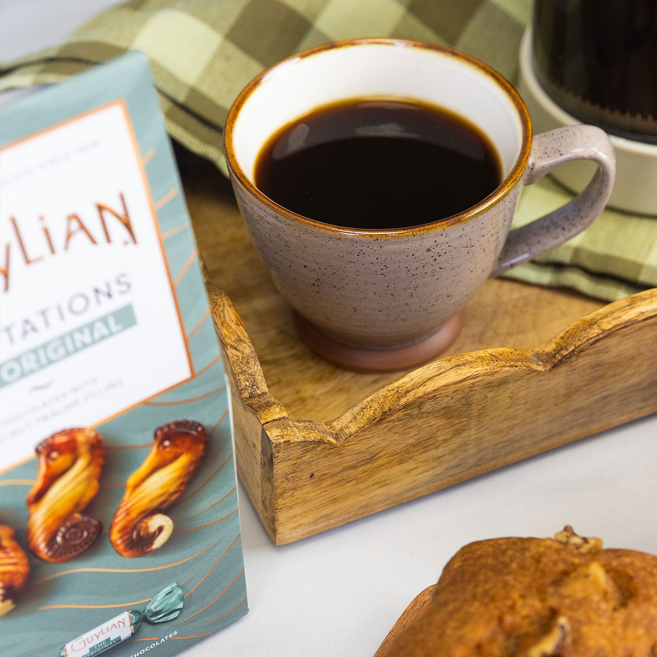 Freshly brewed black coffee served in a speckled ceramic mug on a rustic wooden tray with Guylian chocolates and a cafetière nearby.