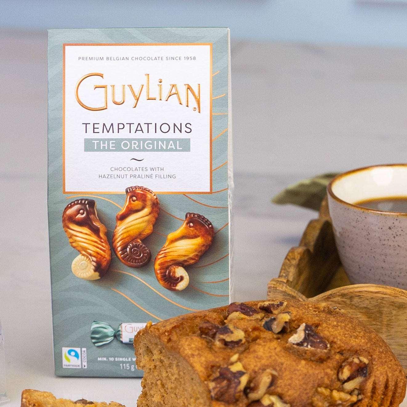 Box of Guylian Temptations Original Belgian chocolates with hazelnut praline filling, displayed alongside walnut loaf cake and a fresh cup of coffee.