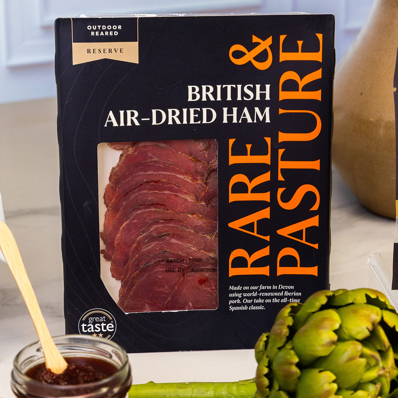 Pack of British reserve air-dried ham with thinly sliced cured pork, presented alongside fresh artichokes and quince fruit cheese.