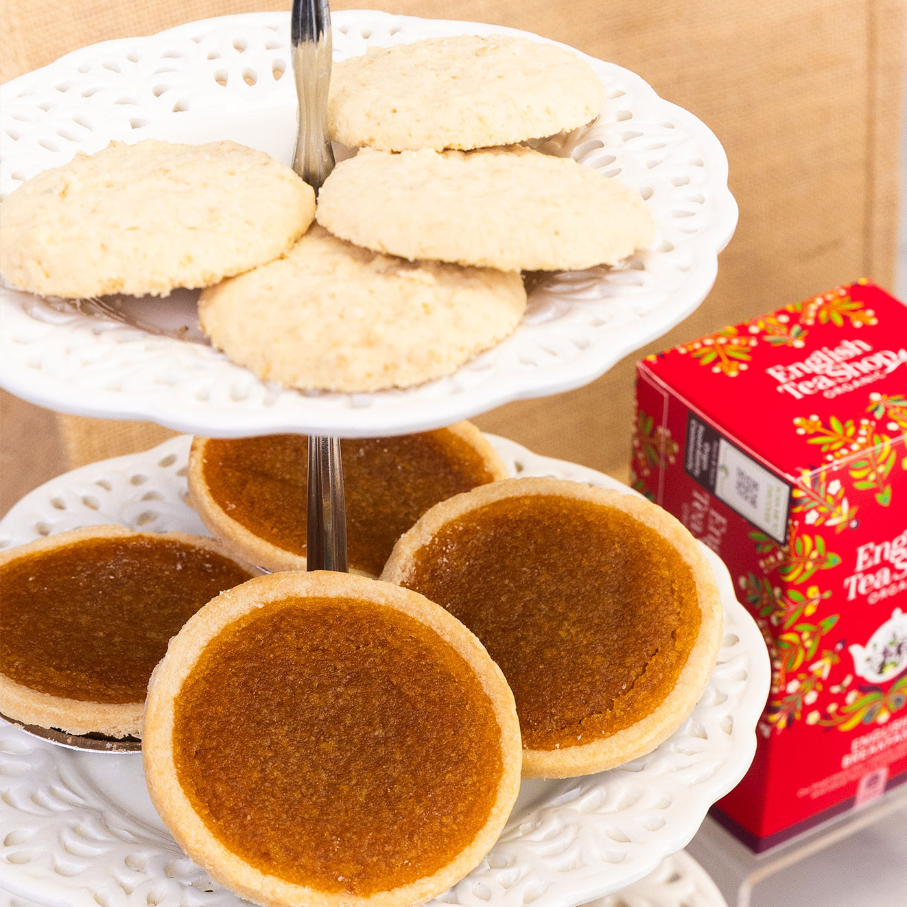 Selection of traditional deep-filled treacle tarts and buttery biscuits arranged on a tiered cake stand beside English Breakfast tea.