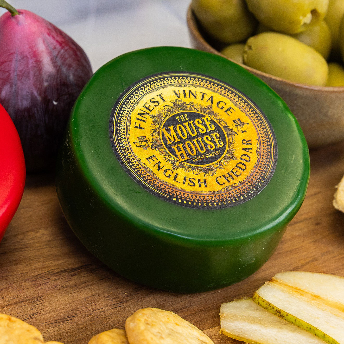 Mouse House Finest Vintage English Cheddar truckle in green wax, presented with crackers, pear slices, olives and fresh fruit.