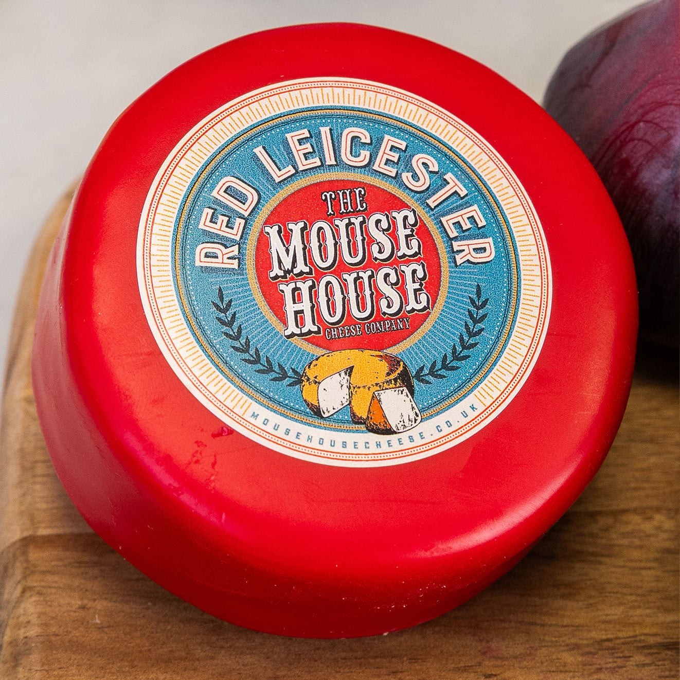 Mouse House Red Leicester waxed cheese truckle presented on a wooden board with oat biscuits and fresh fruit.