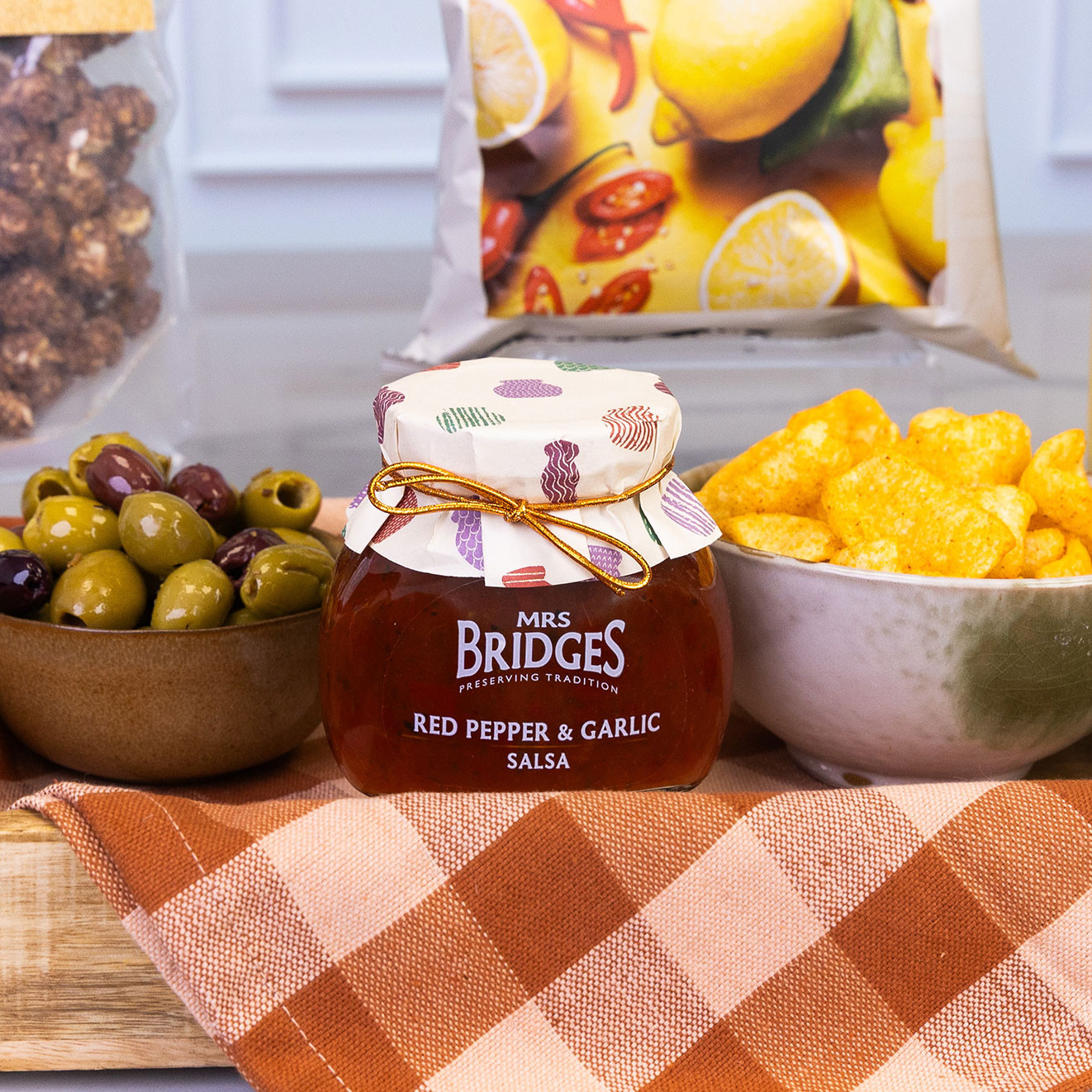 Mrs Bridges Red Pepper & Garlic Salsa served alongside mixed olives and crunchy hummus chips for sharing.