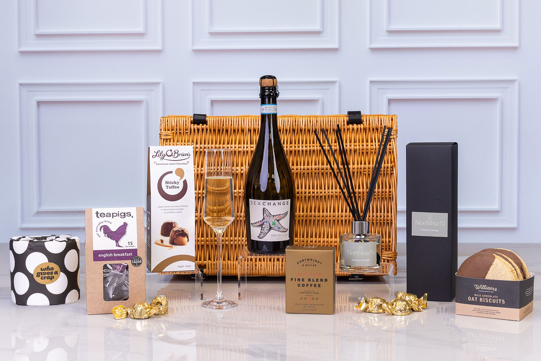 Luxury gift hamper presented in a wicker hamper with Prosecco, artisan chocolates, tea, coffee, chocolate oat biscuits, reed diffuser and premium toiletries.