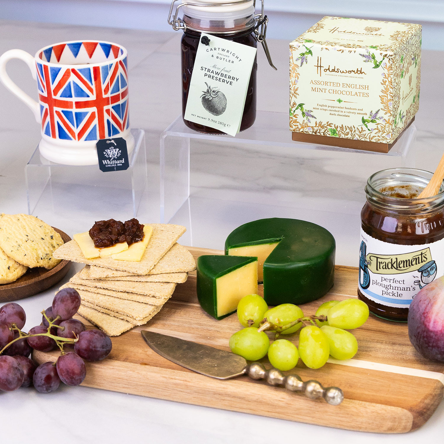 Close up of the Traditional British afternoon tea gift hamper featuring Earl Grey tea, fruit cake, mint chocolates, artisan biscuits, vintage cheddar, preserves, crackers, fresh fruit and a Union Jack mug.