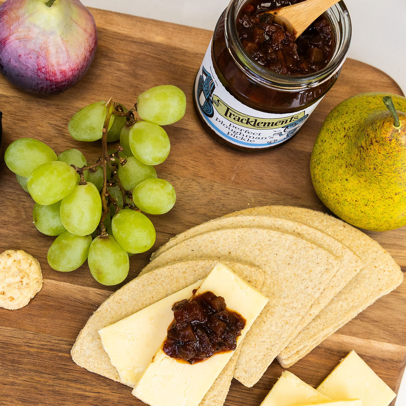 Cheese and crackers served with Tracklements Perfect Ploughman's Pickle, fresh green grapes and pear for a classic savoury pairing.