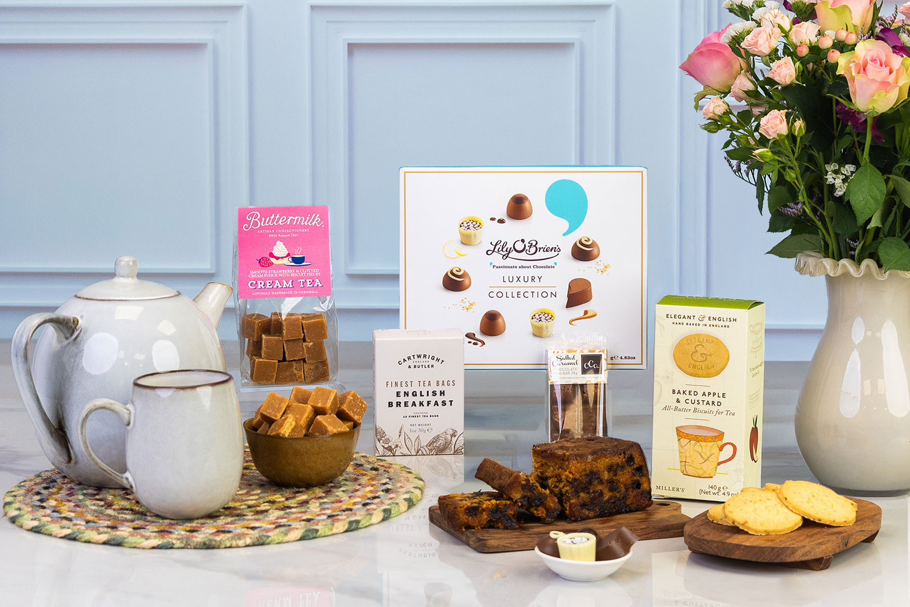 Afternoon tea gift hamper featuring luxury chocolates, English breakfast tea, fruit cake, apple and custard biscuits, cream tea fudge, teapot and fresh flowers.