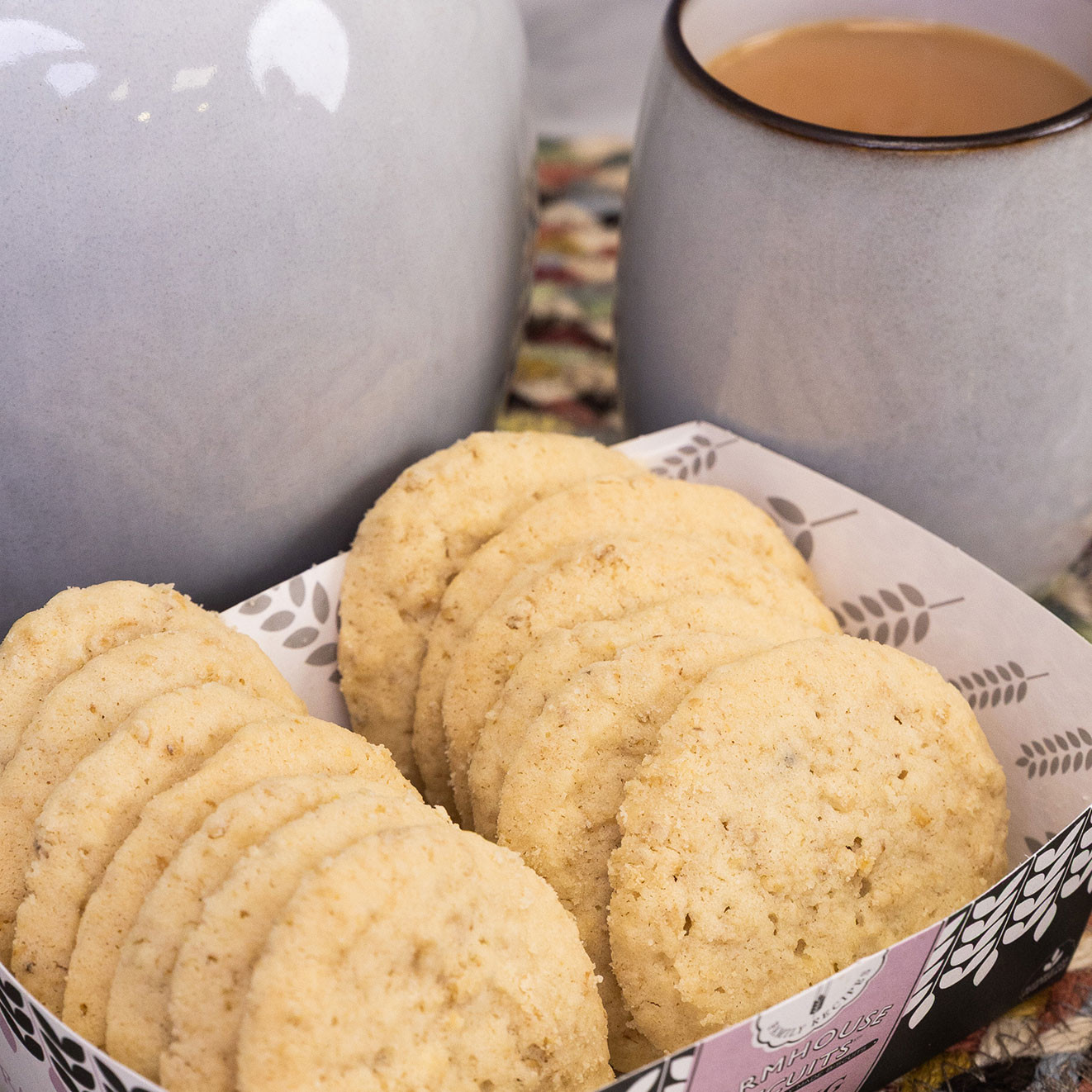 Traditional melting moment biscuits served in a tray alongside a teapot and a freshly poured mug of tea.