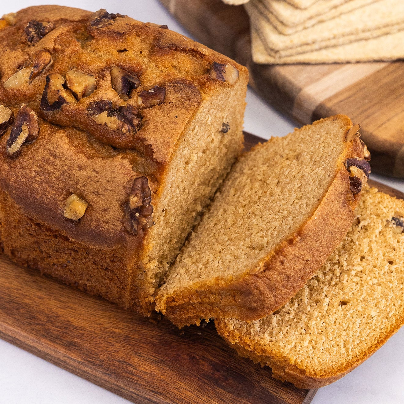 Moist walnut loaf cake sliced on a wooden serving board, topped with crunchy walnut pieces and ready to serve.
