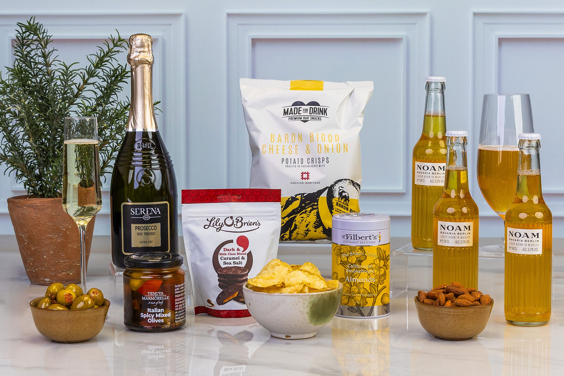 Luxury drinks and snacks hamper featuring Prosecco, Bavarian lager, gourmet crisps, olives, smoked almonds, chocolate discs and savoury nibbles.