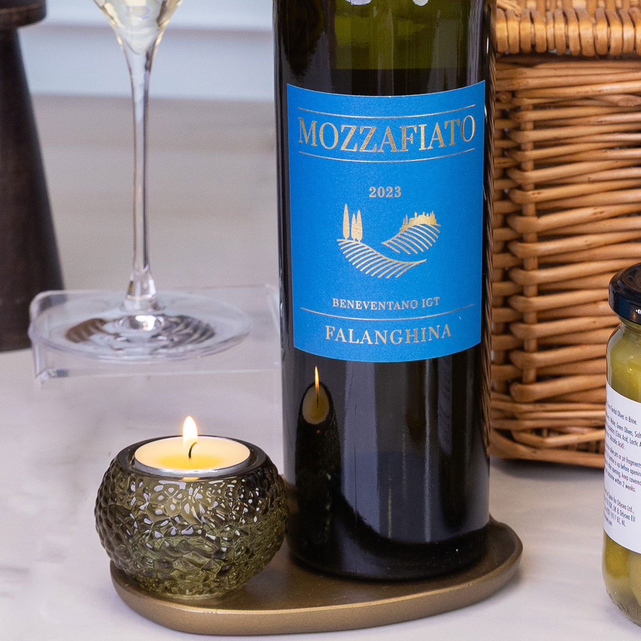Bottle of Mozzafiato Falanghina Italian white wine with a lit candle and glass of chilled white wine for elegant gifting.