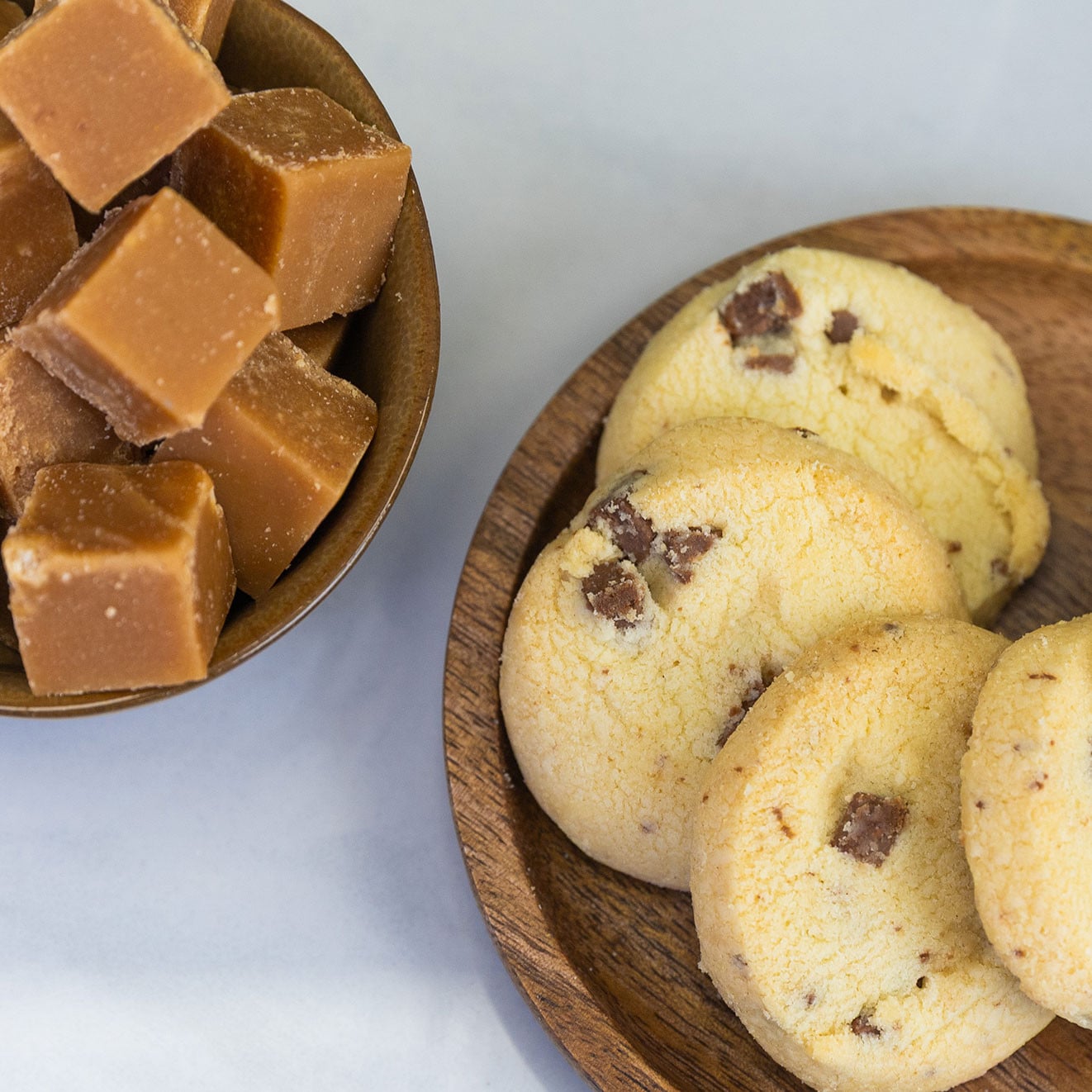 Buttery milk chocolate chunk biscuits served on a wooden plate beside a bowl of creamy fudge cubes, perfect for afternoon tea.