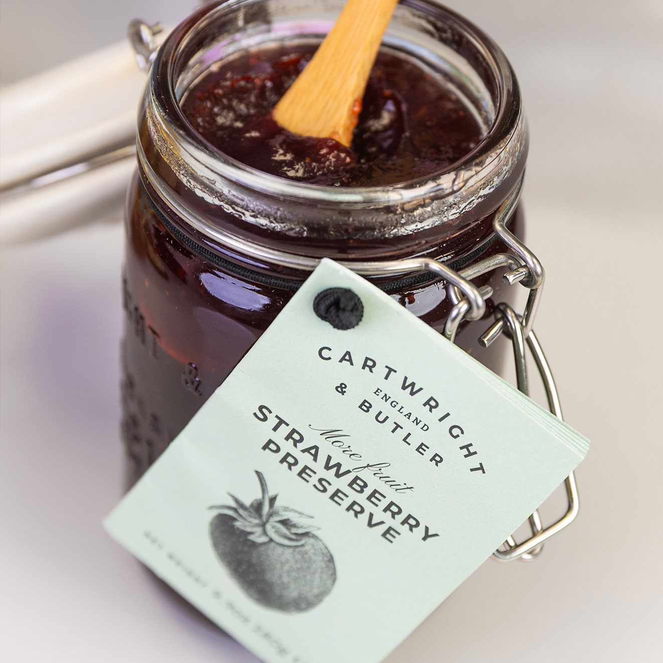 Cartwright & Butler More Fruit Strawberry Preserve in a clip-top glass jar, filled with rich strawberry jam and served with a wooden spoon.