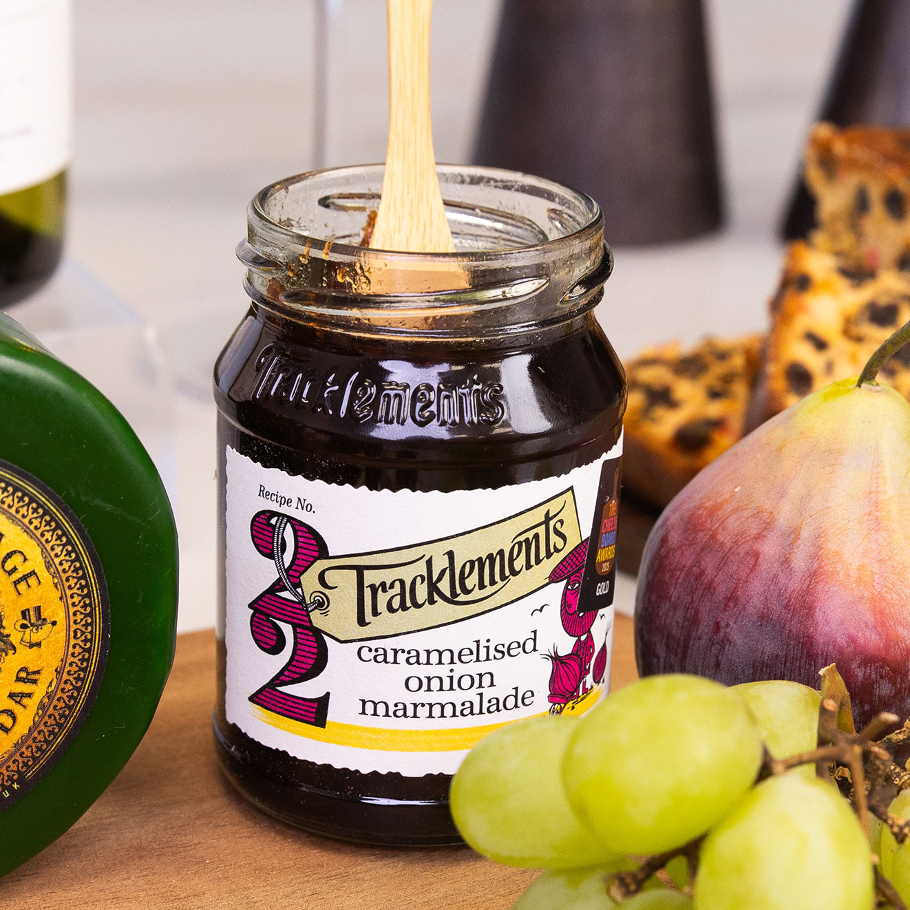 Tracklements Caramelised Onion Marmalade in a glass jar with a wooden spoon, perfect for pairing with mature cheese and crackers.