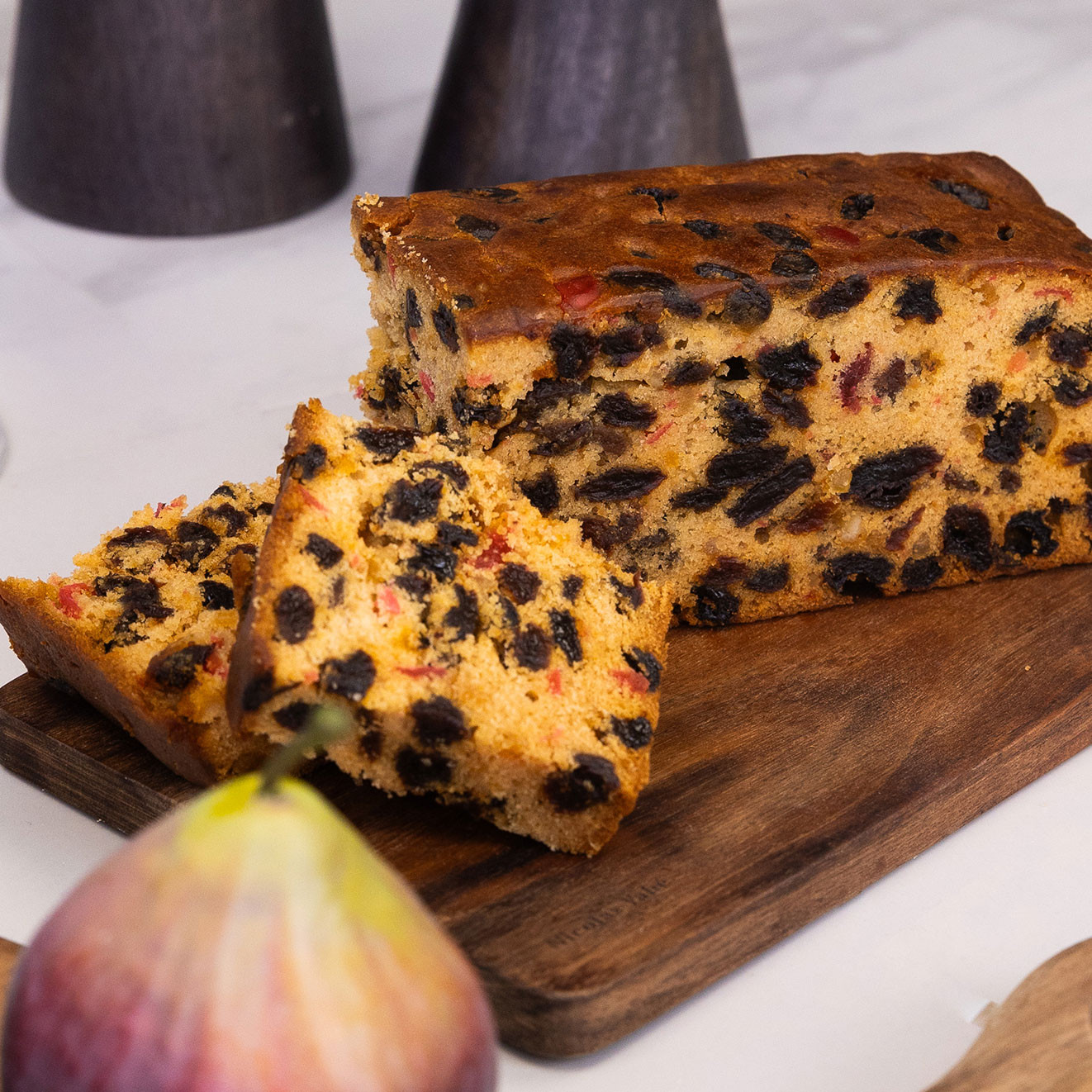 Traditional rich fruit cake packed with raisins and mixed fruit, sliced and presented on a wooden serving board.