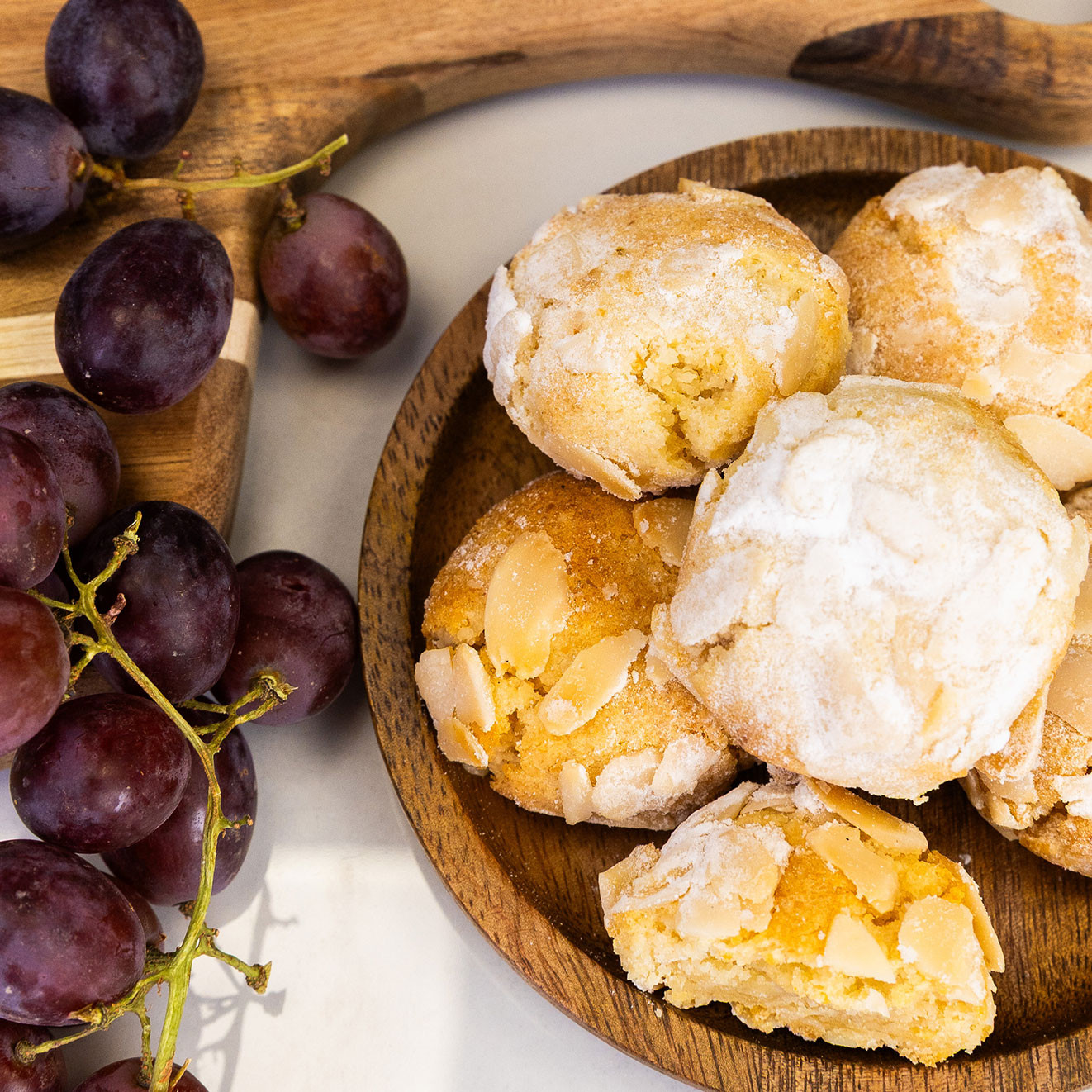 Traditional Italian amaretti biscuits dusted with icing sugar and topped with flaked almonds, served alongside fresh red grapes.