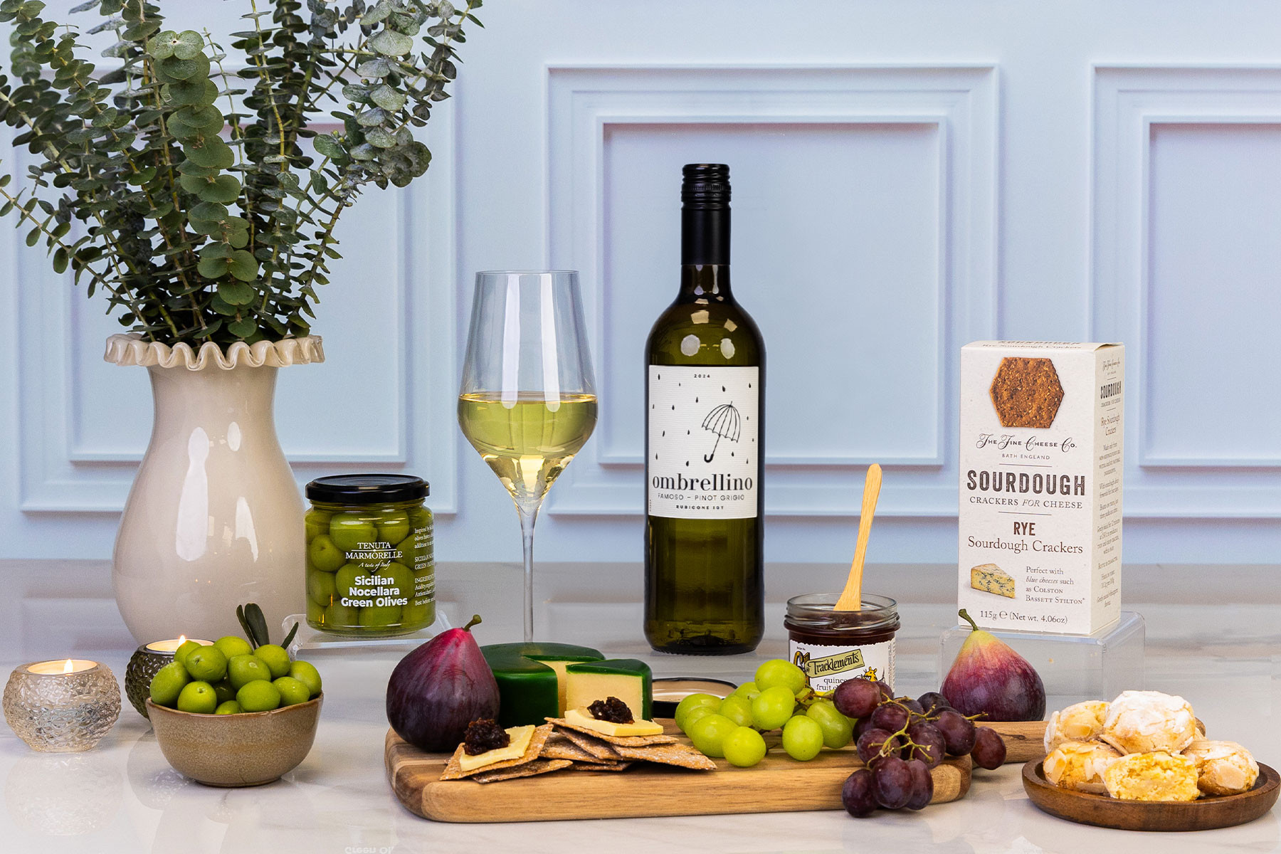 White wine and cheese gift hamper featuring Ombrellino Pinot Grigio, Sicilian green olives, sourdough crackers, quince fruit cheese, artisan cheese, amaretti biscuits and fresh grapes, beautifully presented for entertaining.