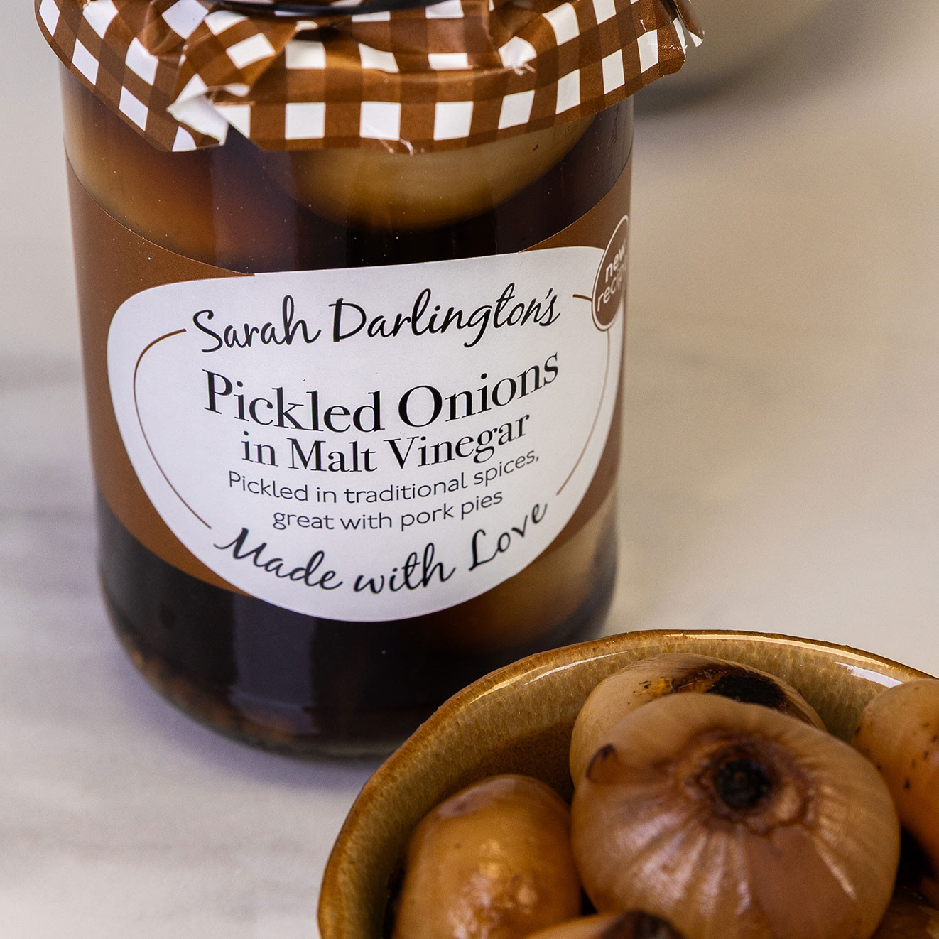 Jar of Sarah Darlington's pickled onions in malt vinegar with a bowl of whole pickled onions, perfect for pairing with cheese and cold meats.