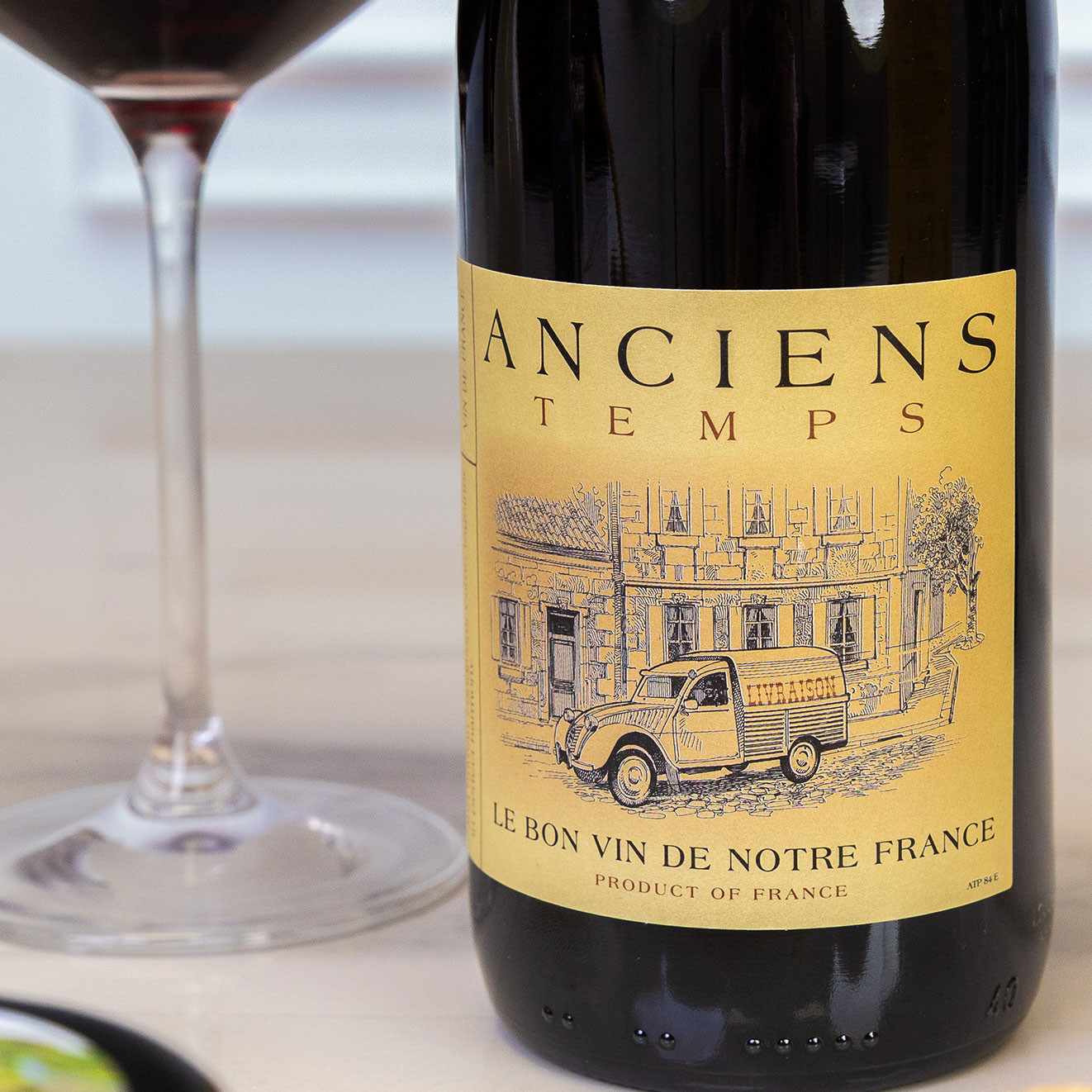 Bottle of Anciens Temps French red wine beside a glass of red wine, offering a classic pairing for cheese boards and savoury nibbles.
