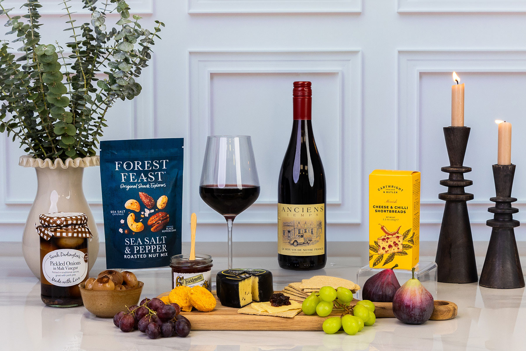Luxury cheese and red wine gift hamper featuring French red wine, mature cheddar, savoury snacks, pickled onions, chutney, crackers and fresh fruit, styled for an elegant evening of entertaining.