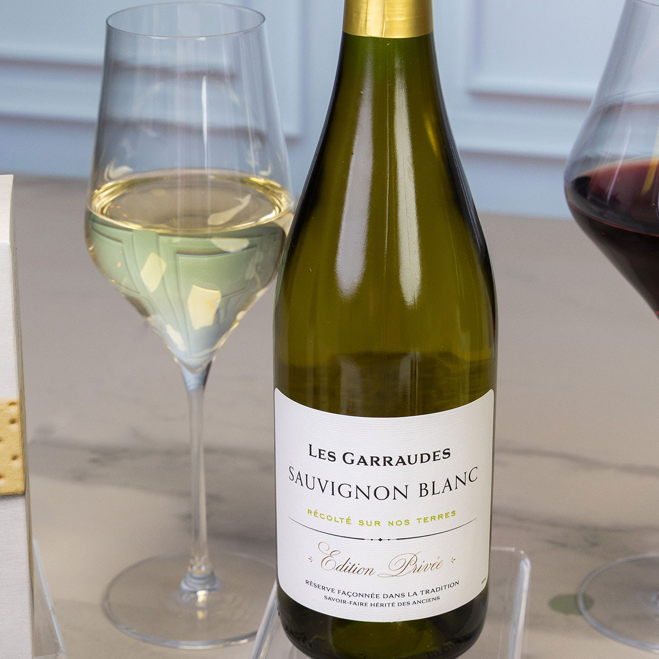 Bottle of Les Garraudes Sauvignon Blanc served beside a glass of chilled white wine, showcasing a crisp French white with fresh citrus and fruit character.