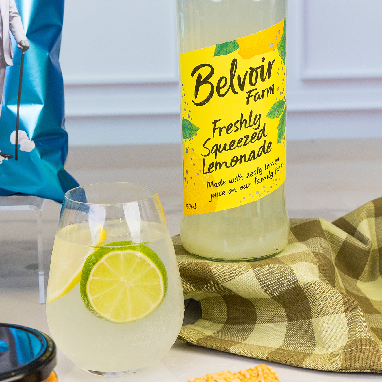 Bottle of Belvoir Farm Freshly Squeezed Lemonade served with a chilled glass garnished with lemon and lime slices, creating a refreshing alcohol-free drink.