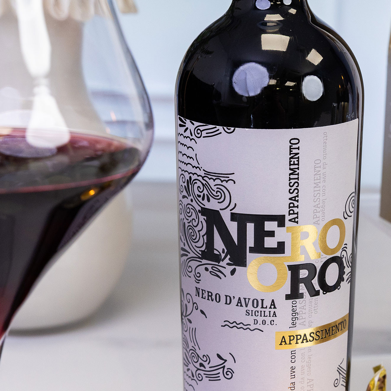 Bottle of Nero Oro Nero d'Avola Appassimento Sicilian red wine beside a glass of red wine, showcasing a rich Italian wine ideal for gifting or special occasions.