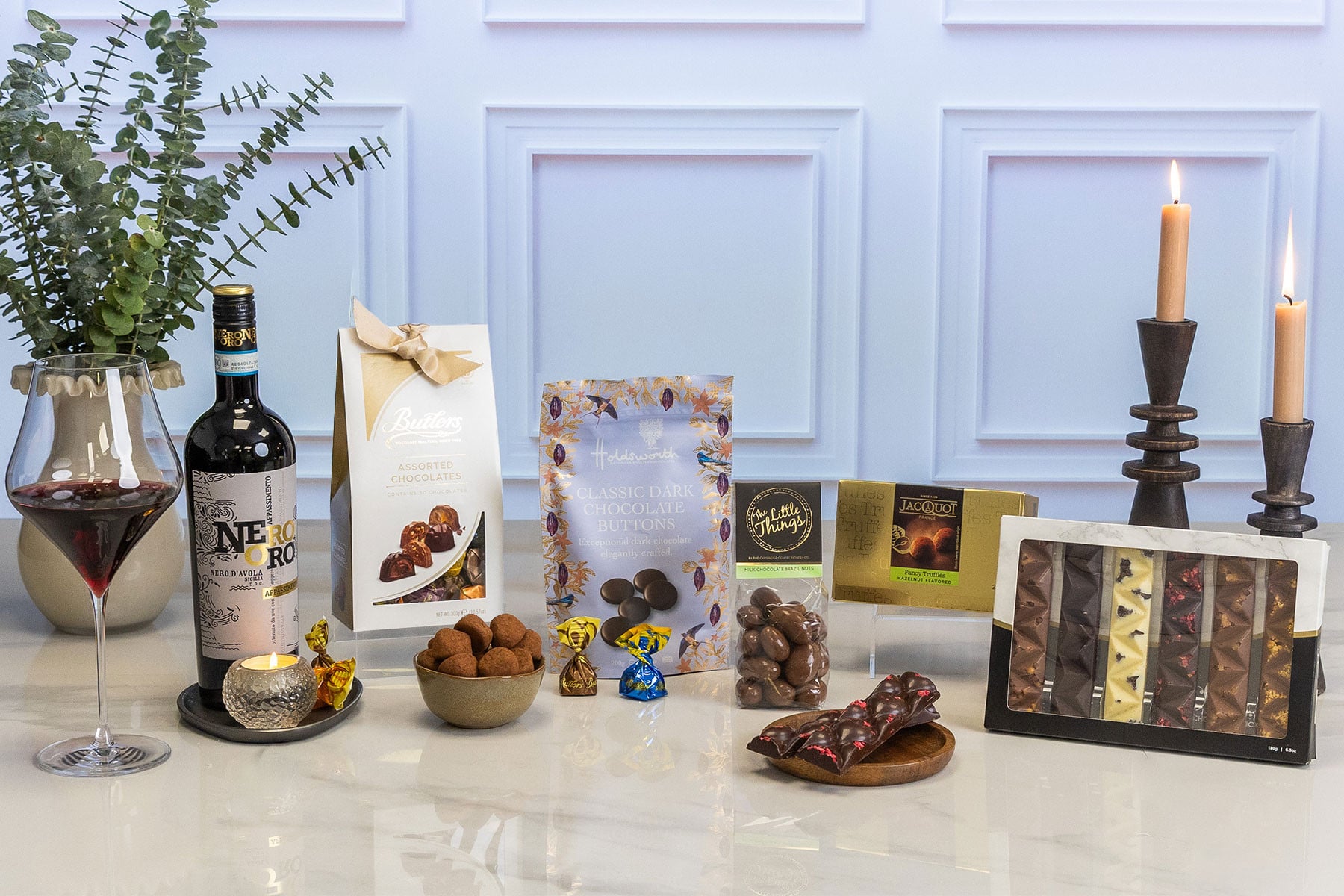 Luxury wine and chocolate gift hamper featuring Nero d'Avola red wine, premium chocolates, chocolate-coated Brazil nuts, hazelnut truffles, artisan chocolate bars and assorted chocolate selection, elegantly presented with candlelight.