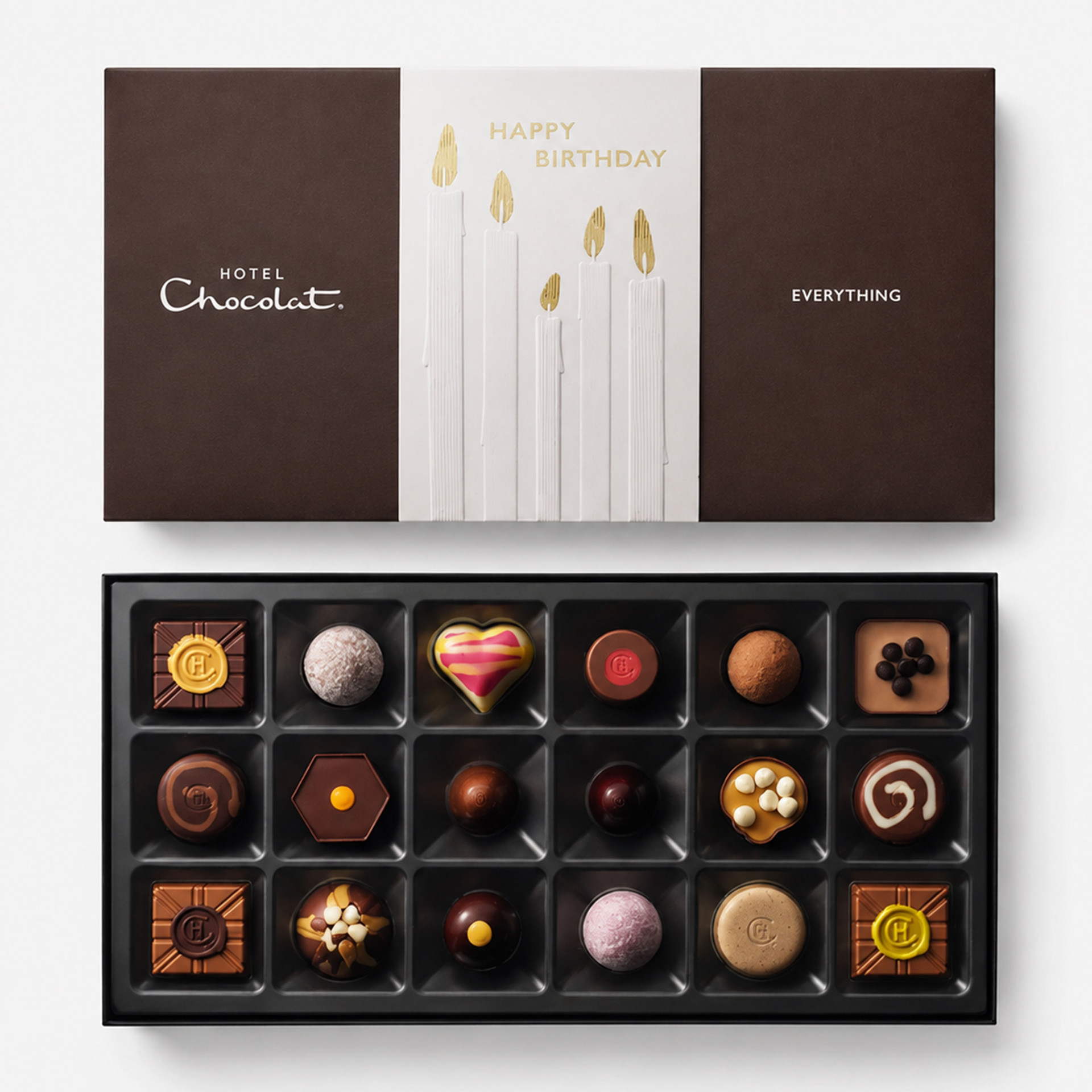 Hotel Chocolat Everything Happy Birthday chocolate collection, shown with a brown and white birthday-themed presentation box featuring gold candles, alongside an open tray of 18 assorted chocolates.