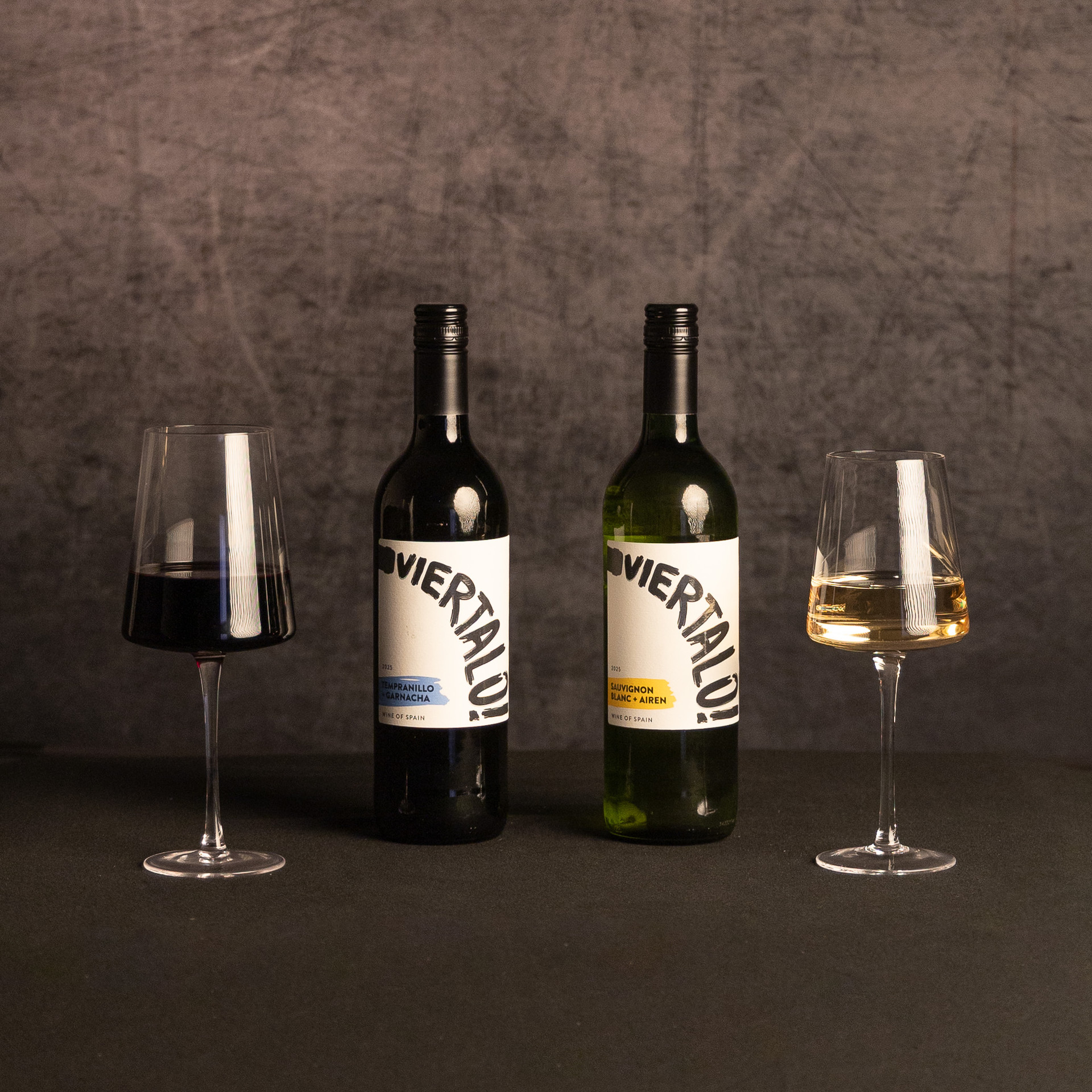 Two bottles of wine—Tempranillo Garnacha and Sauvignon Blanc—stand between glasses of red and white wine against a dark, textured backdrop.