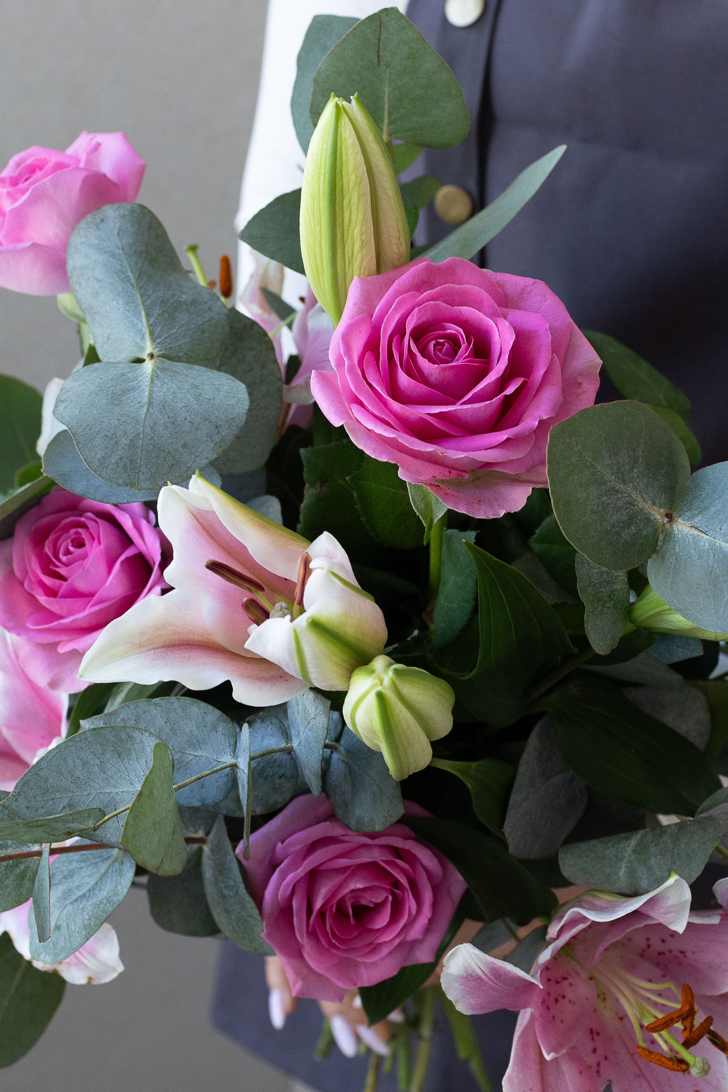 Close-up of pink roses, pink lilies, lily buds, and eucalyptus foliage in a bouquet.
