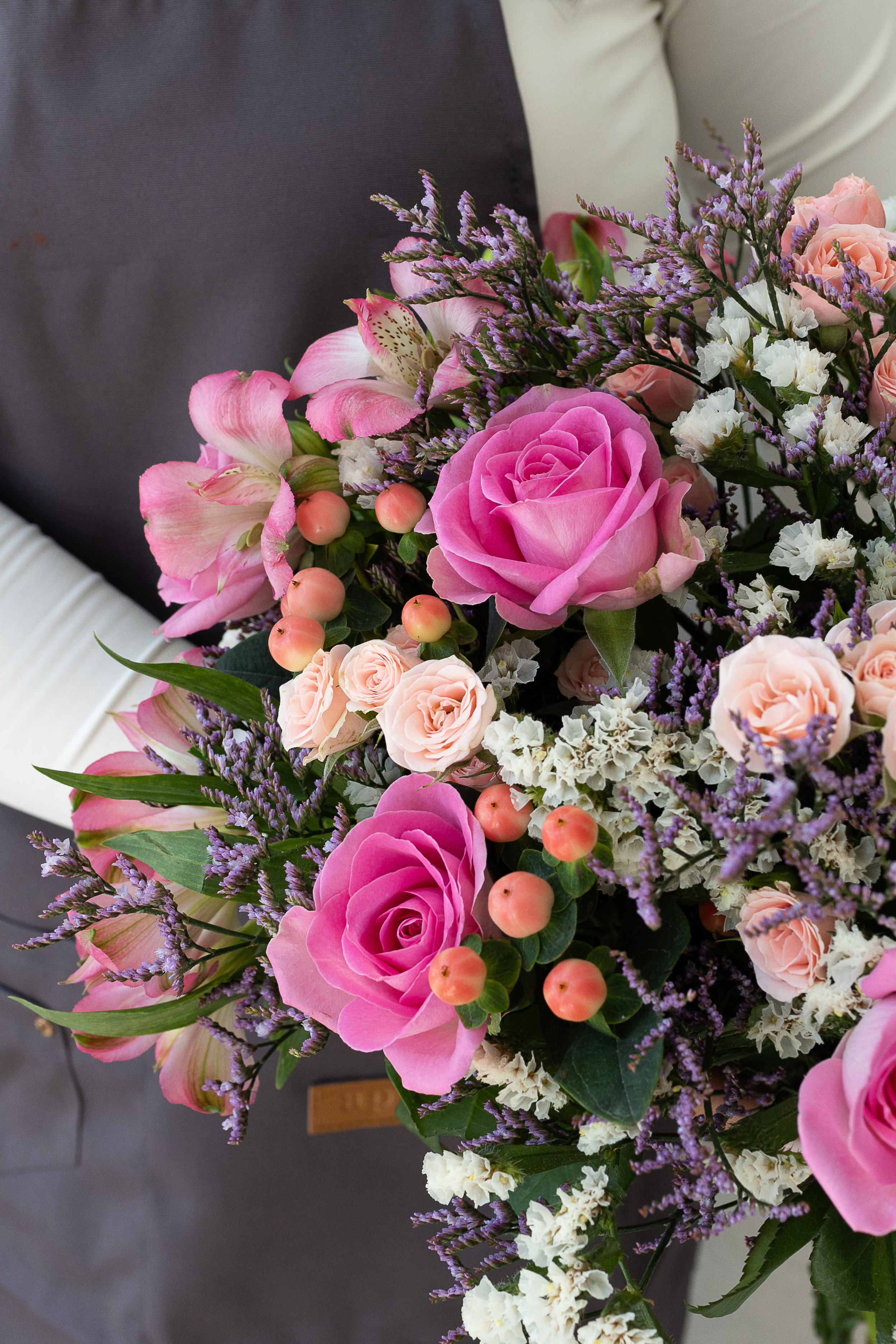 Close-up of pink roses with lilac statice and berries.
