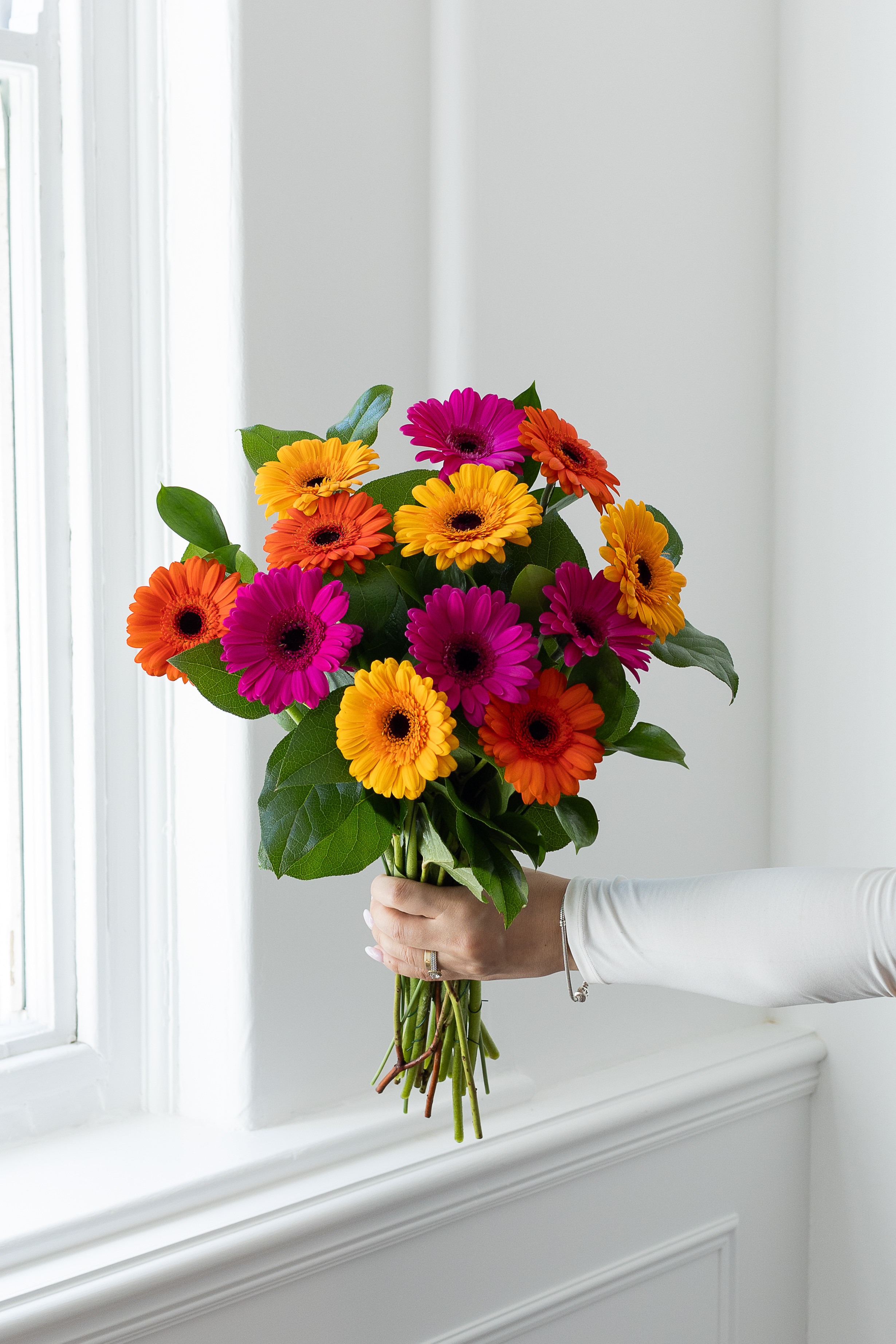 Mixed pink, orange, and yellow gerbera bouquet by a window.